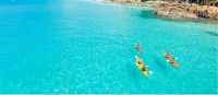 Kayakers paddle turquoise waters off a forested island in the Whitsundays, Queensland.