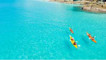 Kayakers paddle turquoise waters off a forested island in the Whitsundays, Queensland.