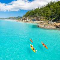 Kayakers paddle turquoise waters off a forested island in the Whitsundays, Queensland.