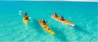 Whitsundays kayakers paddle across turquoise water toward a sandy cay, Queensland.